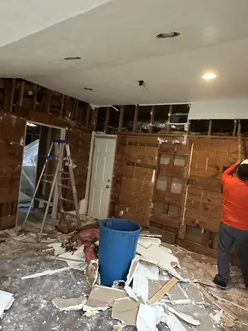 Interior demolition in progress with wall cavities exposed and removed materials on the floor.