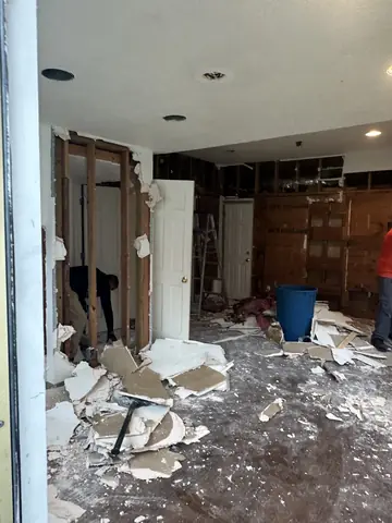 Interior demolition with exposed wall studs, removed drywall, and workers in the work area.