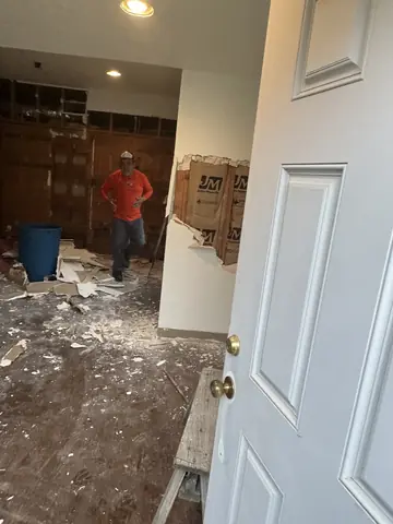 View through an open doorway during demolition, with exposed insulation and removed drywall.