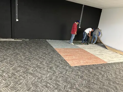 Workers removing existing carpet along the wall of a commercial interior.