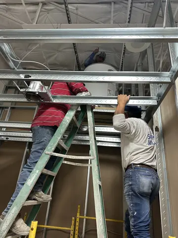 Crew working on overhead framing from ladders.
