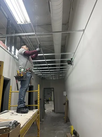 A worker on scaffolding at the ceiling framing of a commercial corridor.