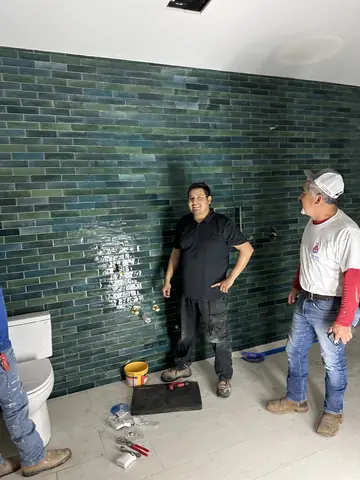 Green-tile bathroom walls, workers, and tools during interior finishing.