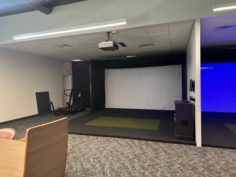 Finished indoor golf-simulator bays with screens and putting turf.