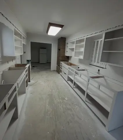 Galley kitchen during remodeling, with cabinet frames and subfloor exposed.