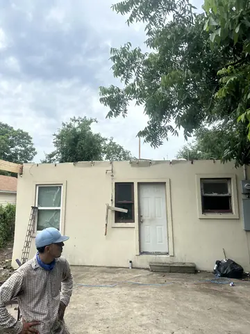 Residential exterior with the roof removed and a worker in the foreground.