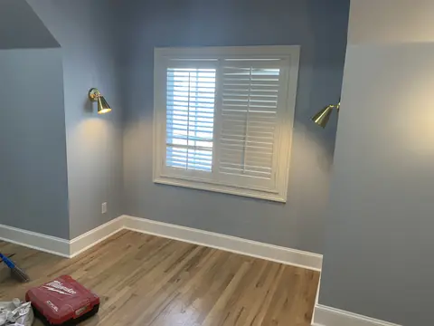 Finished room with gray walls, a shuttered window, wall sconces, and wood flooring.