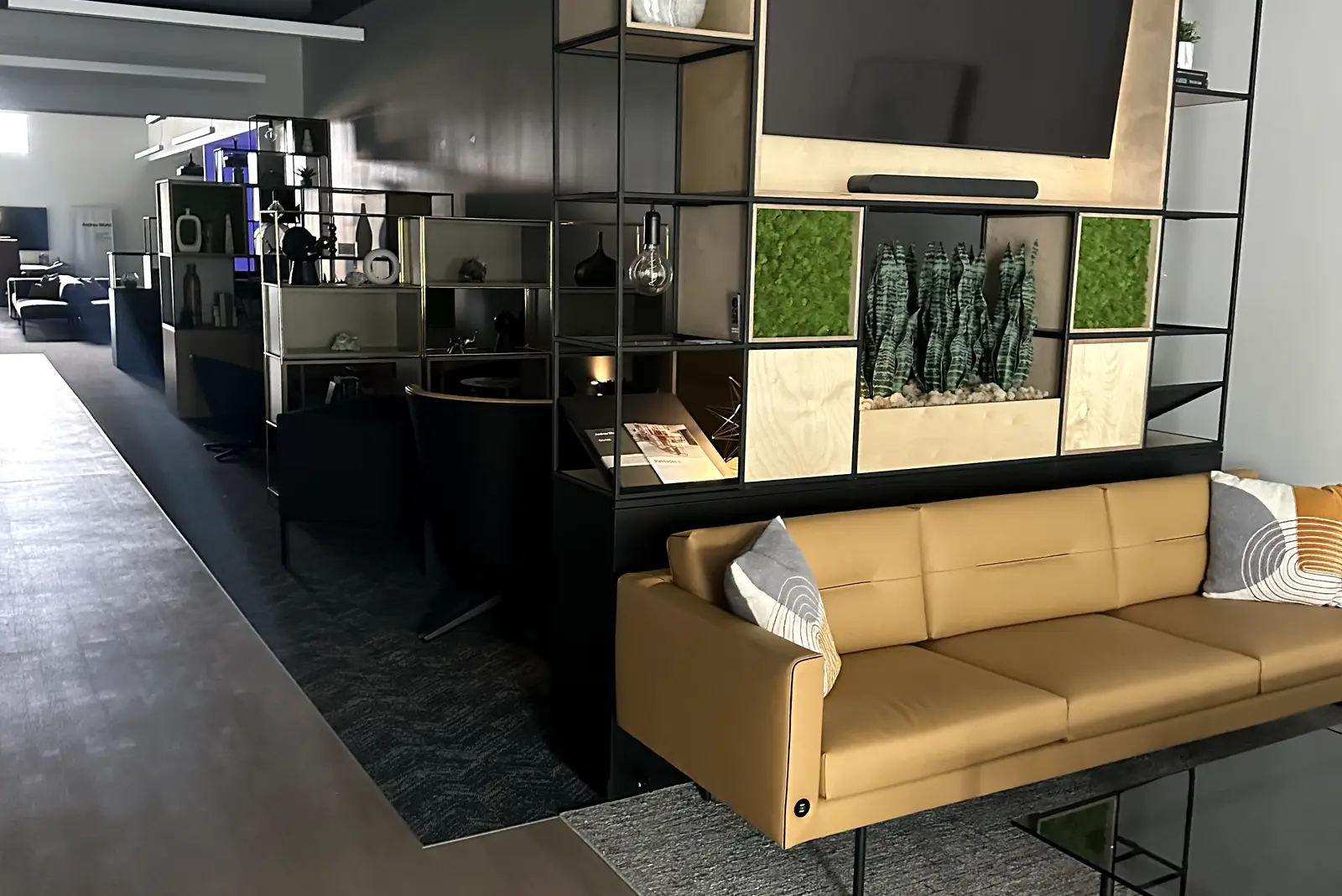 Finished commercial lounge with a camel leather sofa, blackened-steel shelving, and a wood media wall — a Melada build-out
