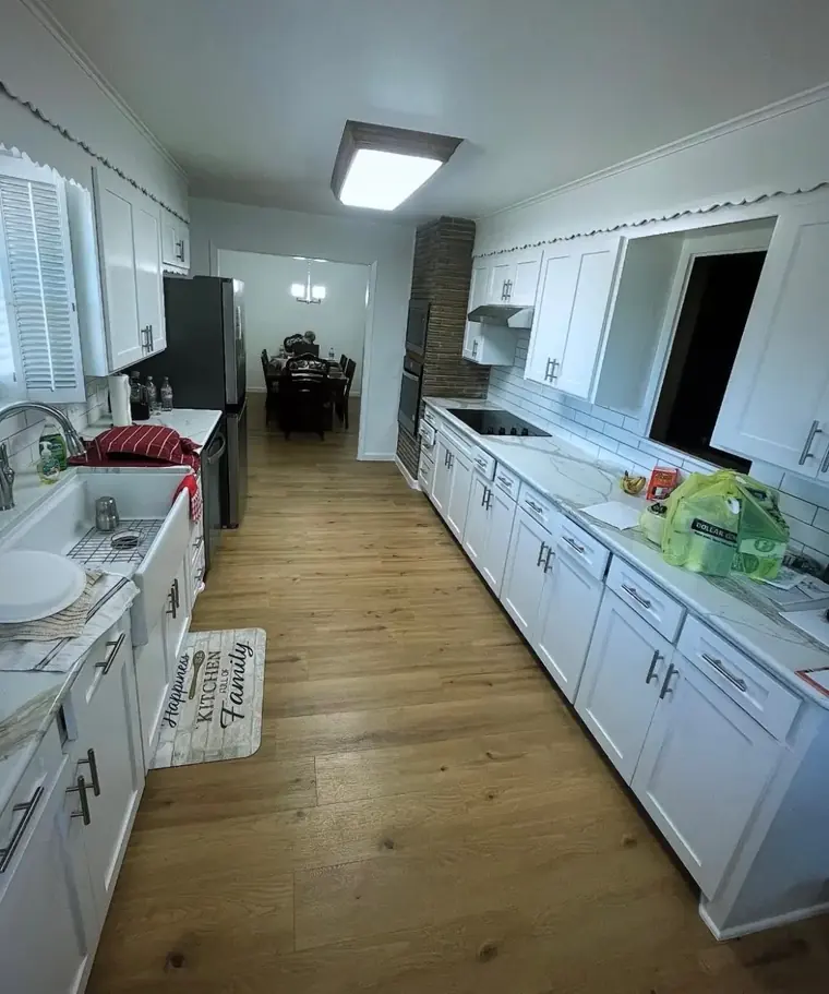 Remodeled galley kitchen with white shaker cabinets, marble-look countertops, and wood-look flooring